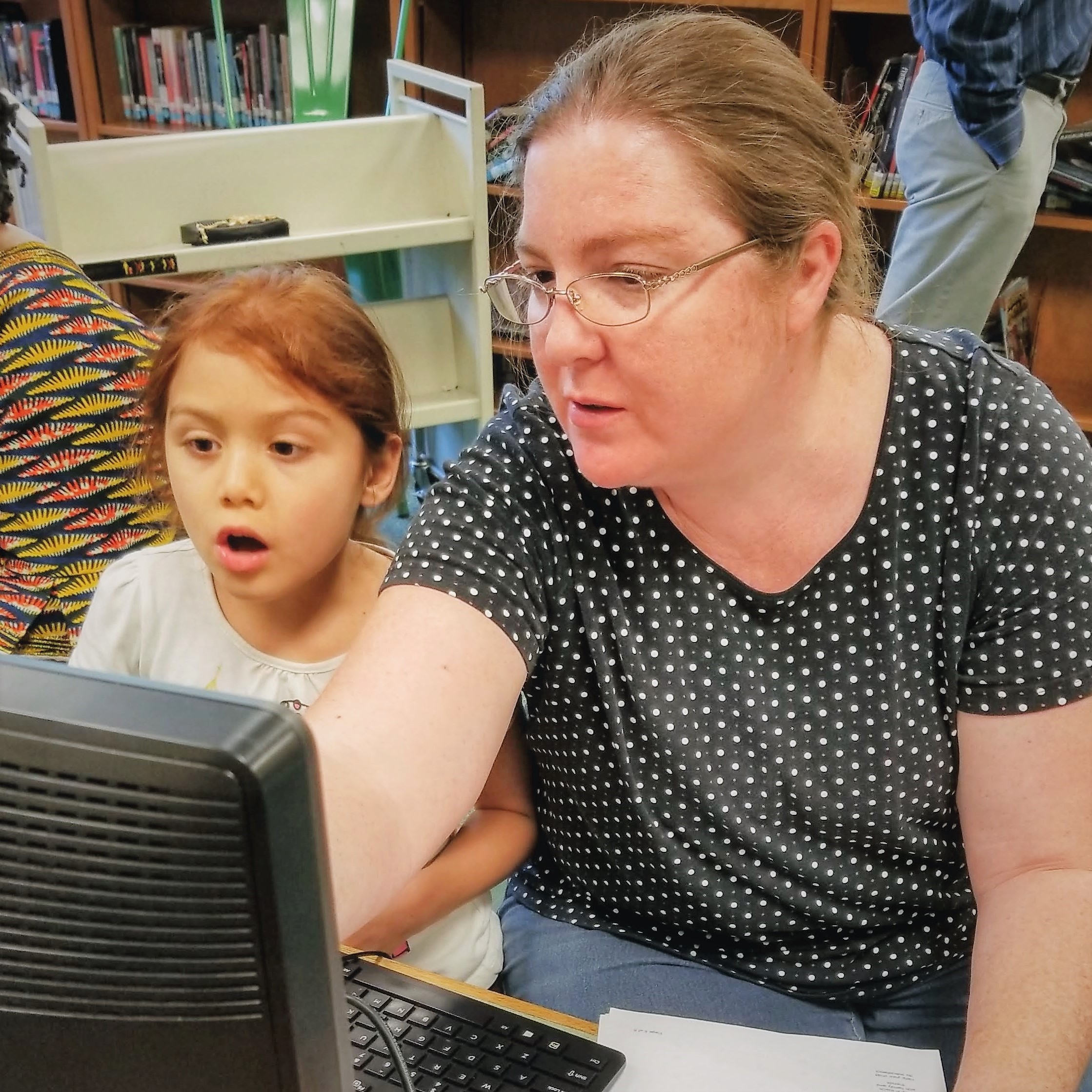 Adult with glasses and child looking a computer together
